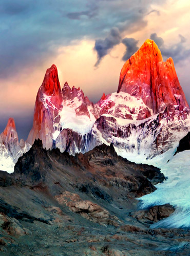Picos graníticos del Monte Fitz Roy iluminados por la luz naranja del atardecer con nubes dramáticas y base de glaciares.